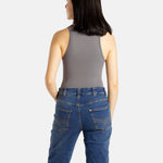 The back of a white woman with long black hair and hoop earrings wears a black tank top and denim jeans.