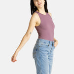 A white woman with long black hair and hoop earrings wears a mauve tank top and denim jeans.