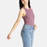 A white woman with long black hair and hoop earrings wears a mauve tank top and denim jeans.