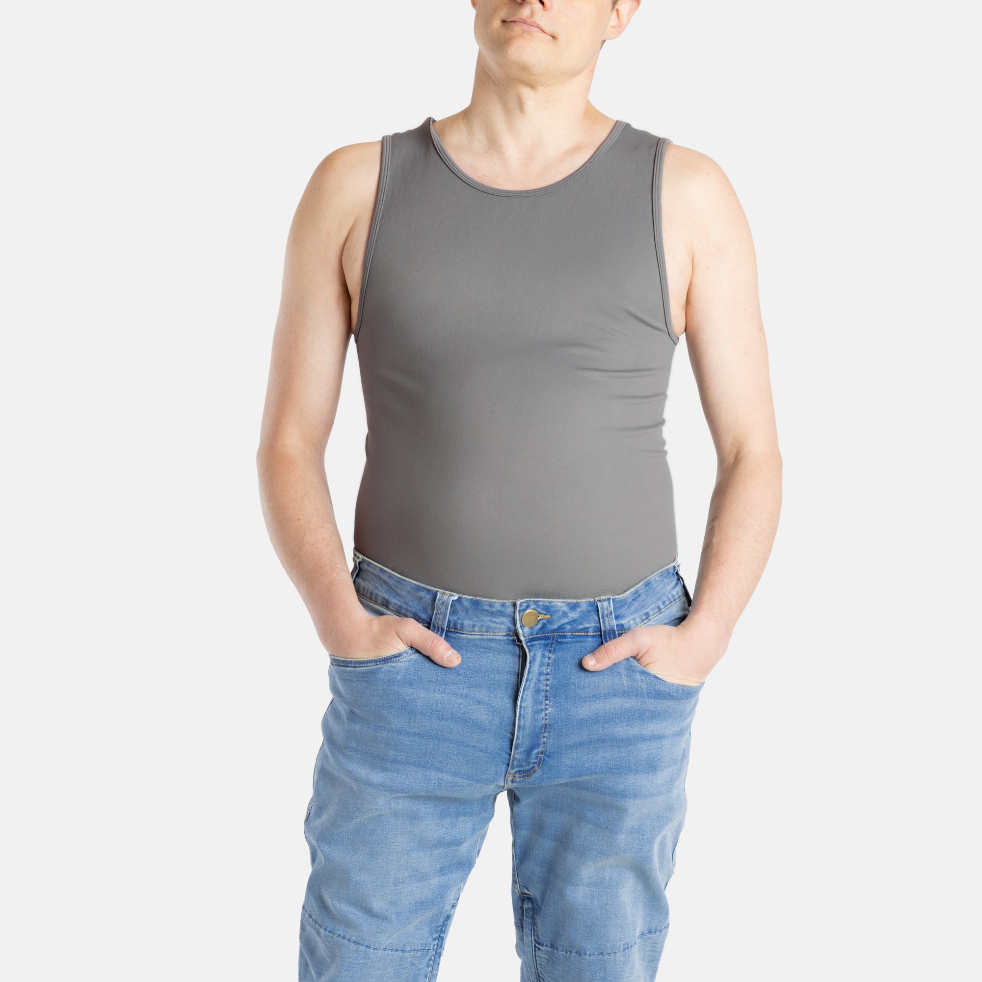 A white man with short brown hair wears a charcoal-gray tank top and denim jeans.