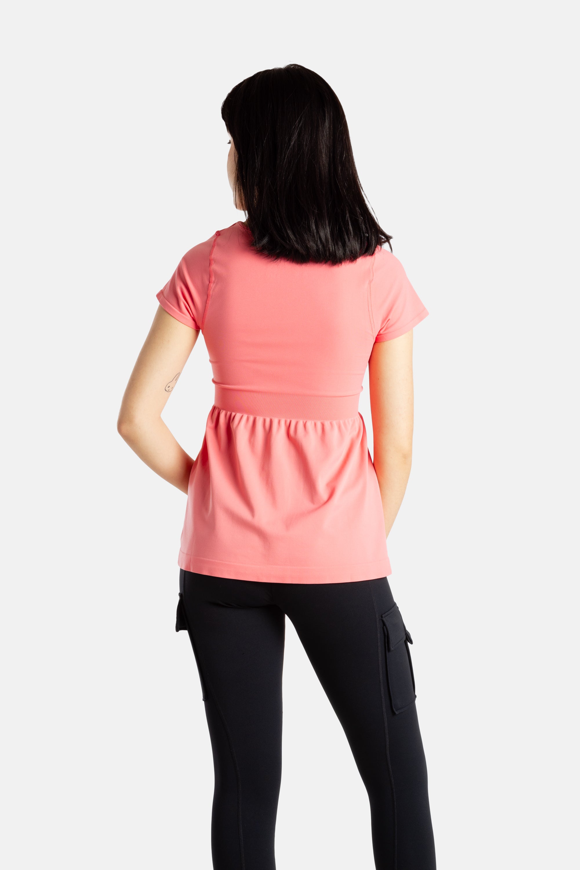 The back of Sophia (A woman with long black hair), wearing the No Limbits Adaptive Women's Coral Sensory Blouse with black leggings.