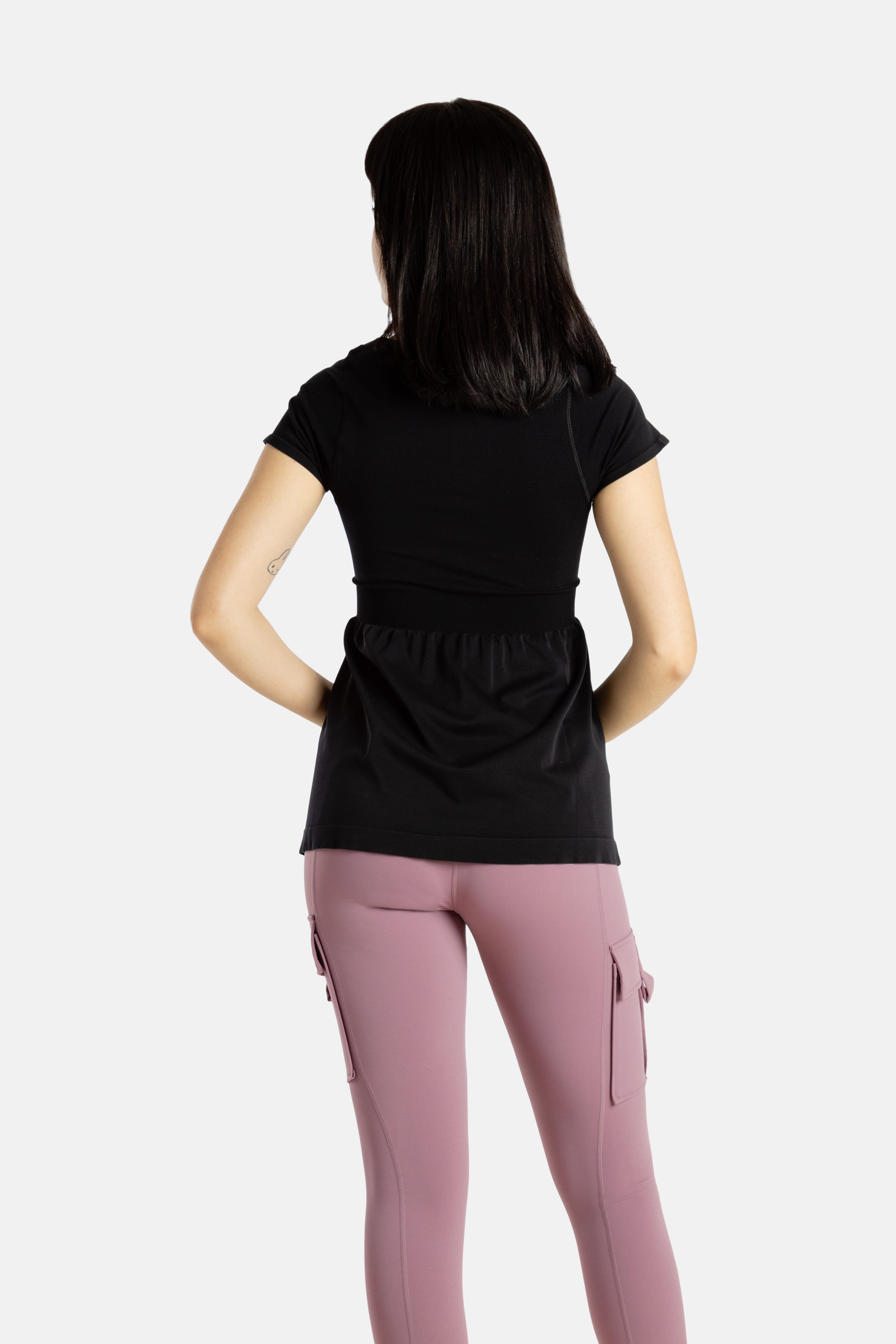 The back of Sophia (A woman with long black hair),wearing the No Limbits Adaptive Women's Black Sensory Blouse with mauve leggings.