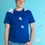 Aqua blue background. A white man with short brown hair wears a navy t-shirt. There are white feathers around him.