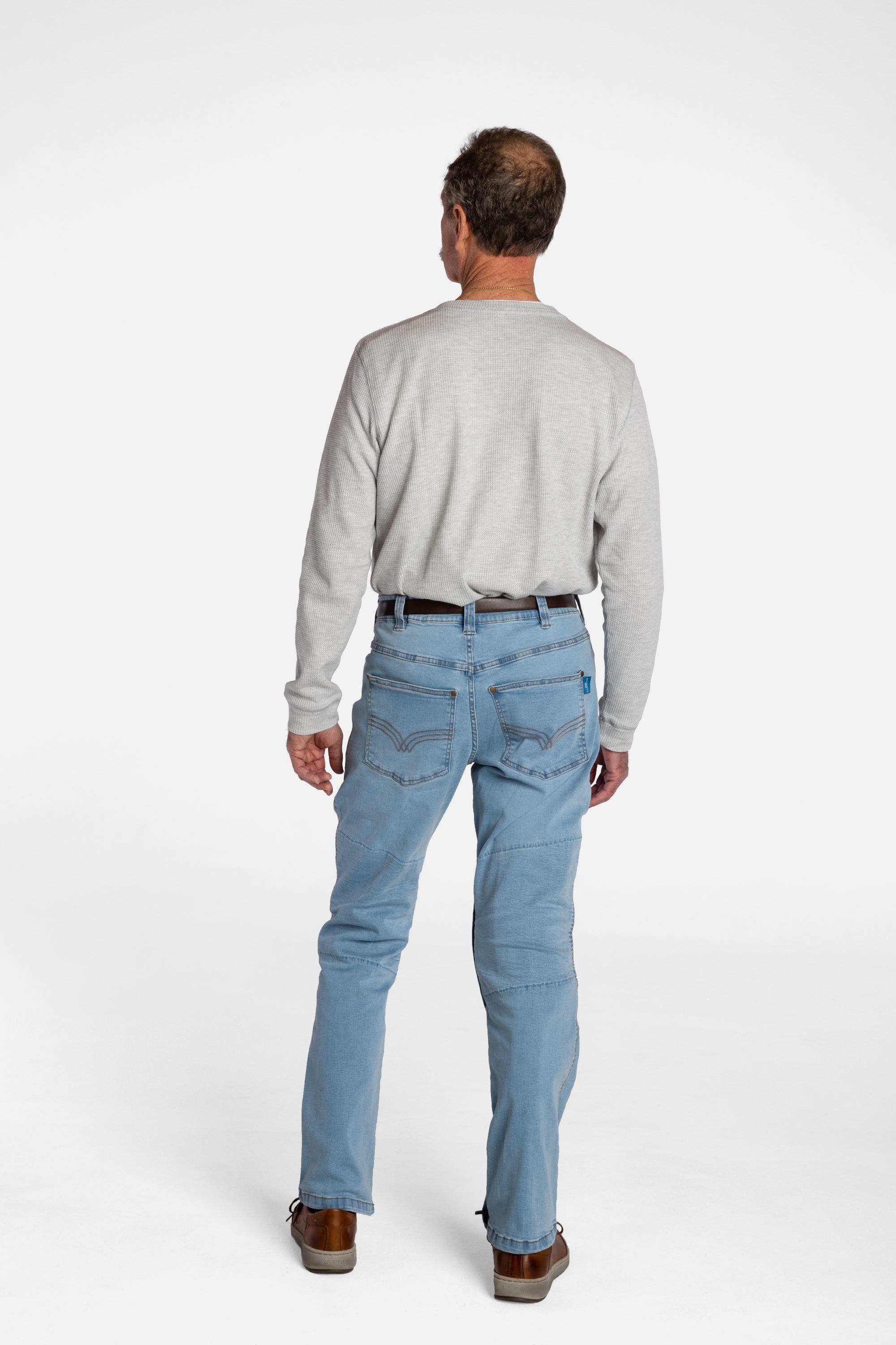 The back of a white, elderly man with a mustache wearing the Men’s Light Wash Unlimbited Pants, with a long-sleeved gray shirt, a brown belt, and brown shoes.