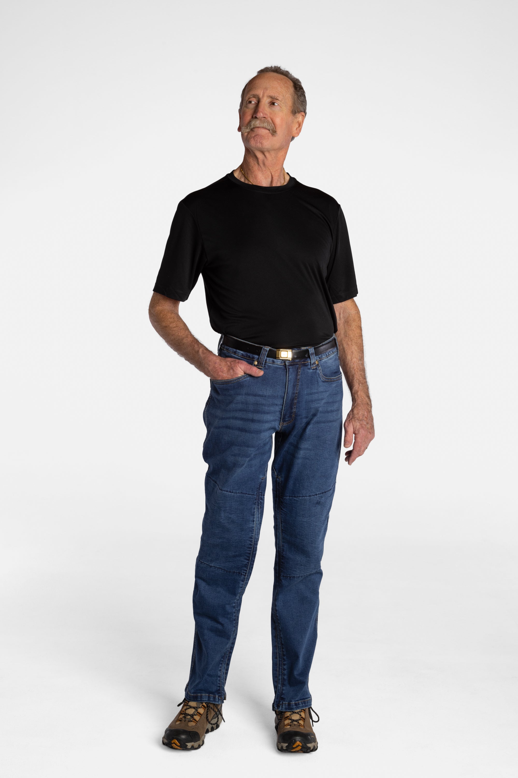 A white, elderly man with a mustache wears the No Limbits Adaptive Men's Dark Wash Unlimbited Pants (which looks like denim jeans), with a black shirt, a brown belt, and brown shoes.