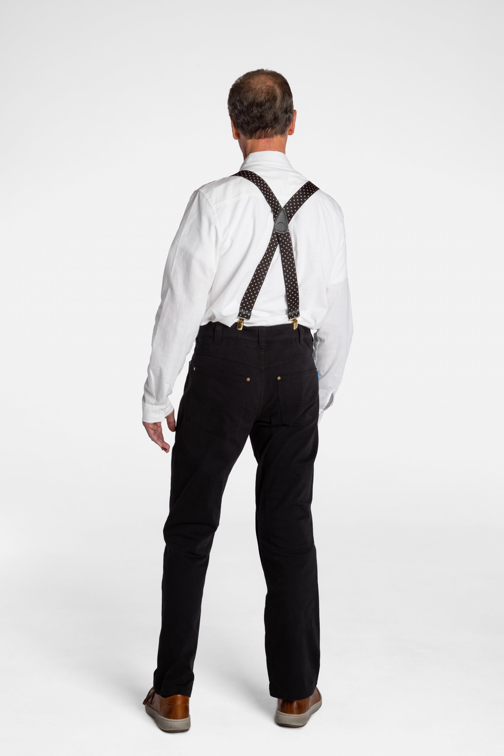 The back of a white, elderly man, wearing the No Limbits Adaptive Men's Black Unlimbited Pants, with a white shirt, brown suspenders, and brown shoes.