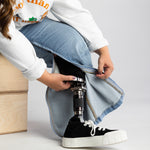 The zipper of the  No Limbits Adaptive Women's Light Wash Unlimbited Pants is zipped up to reveal a prosthetic leg  on the wearer.