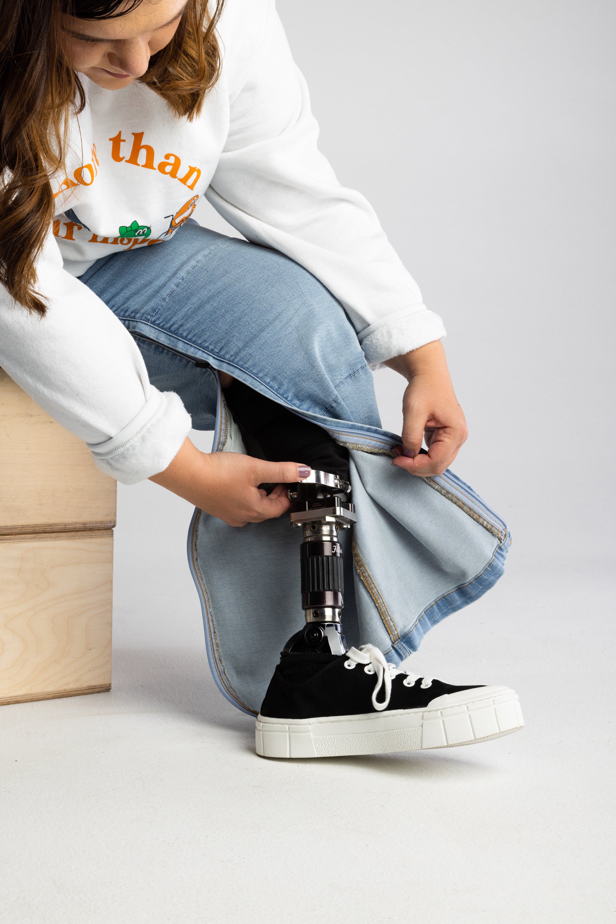 The zipper of the  No Limbits Adaptive Women's Light Wash Unlimbited Pants is zipped up to reveal a prosthetic leg  on the wearer.