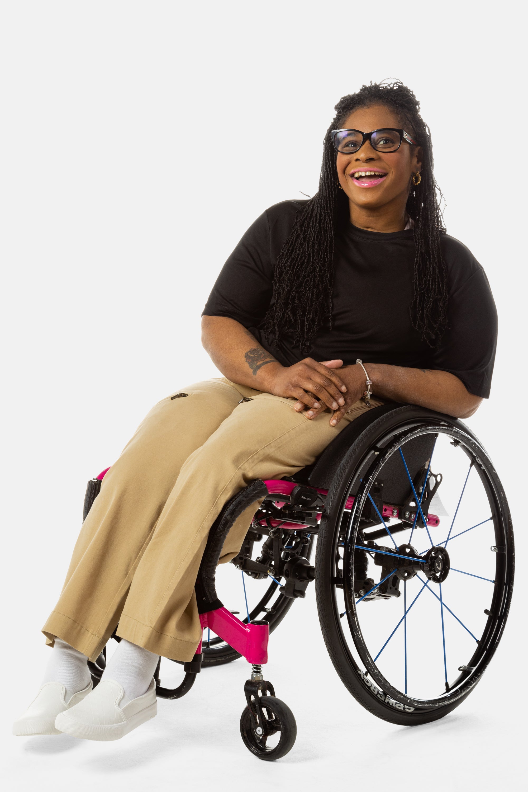 Princess, a Black woman on a pink wheelchair (with long locs, light pink lipstick, clear black sunglasses, and hoops) wears the No Limbits Adaptive Women's Khaki Wheelchair Pants.