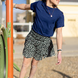 A little girl is wearing a navy blue crewneck t-shirt. She is wearing a black and white skirt with black and white shoes. She is also standing on a jungle gym.