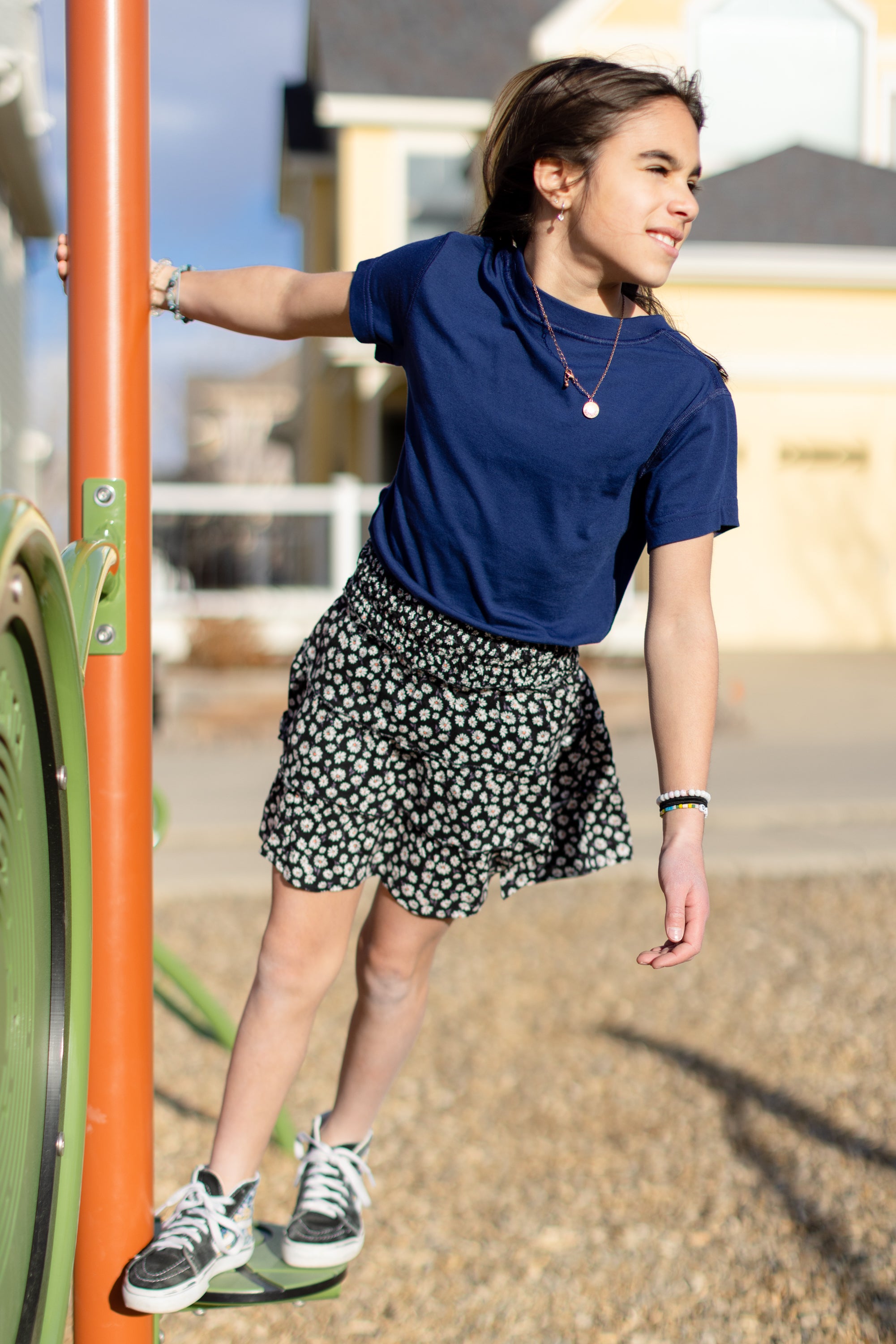 A little girl is wearing a navy blue crewneck t-shirt. She is wearing a black and white skirt with black and white shoes. She is also standing on a jungle gym.