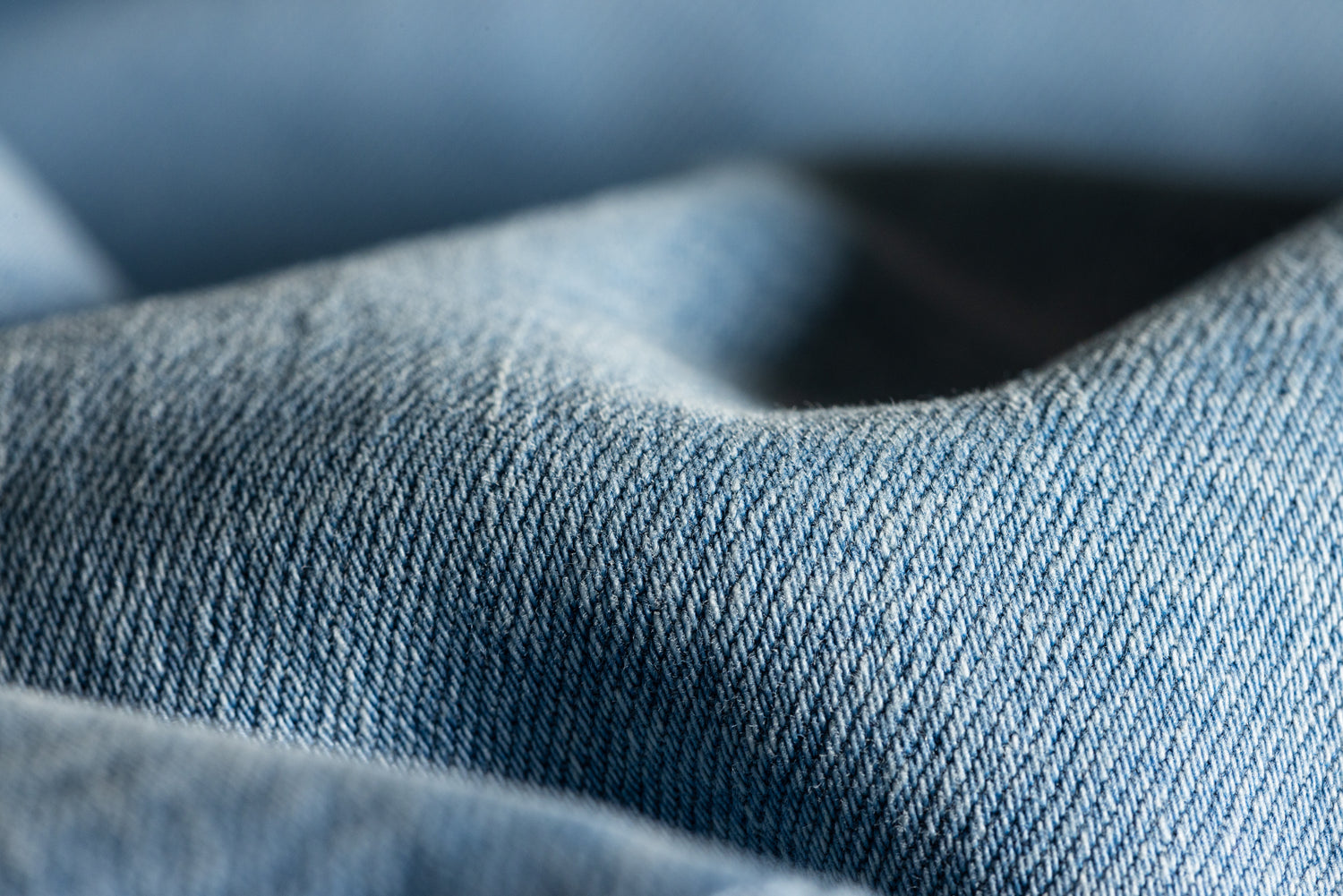 A close up of light wash denim jeans. It is so zoomed in that you can see the stitching of the jeans.