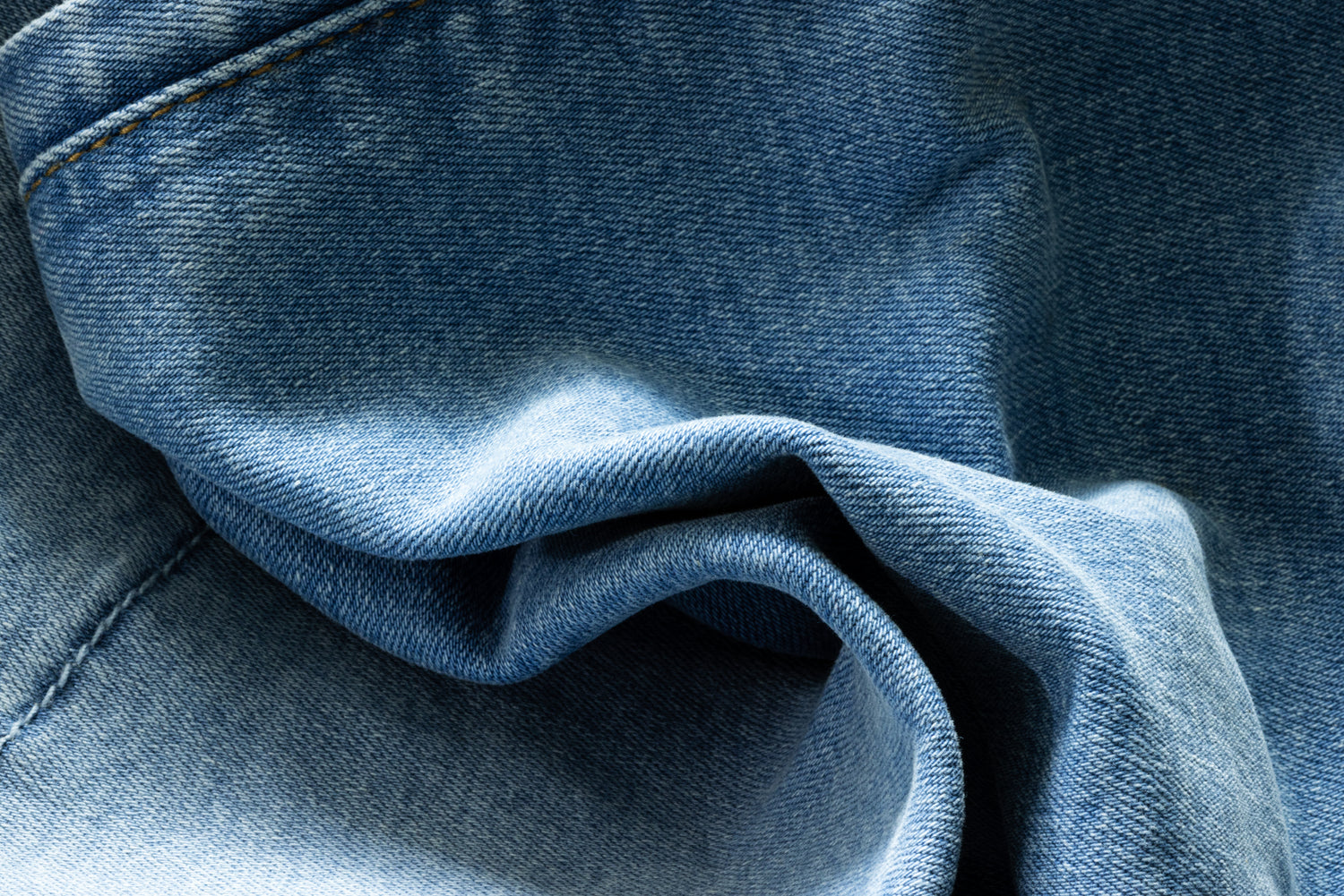 A close up of light wash denim folded, you can see the stitching on it. 