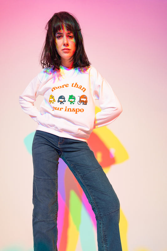 Sophia (A Latina woman with long black hair) poses in front of a white wall. There are outlines behind her that are light blue, purple, pink, and yellow. She is wearing a white sweater that says “not your inspo with the four No Limbits crew members (Colorful circles with forearm crutches, a prosthetic leg, and a wheelchair), and denim jeans.