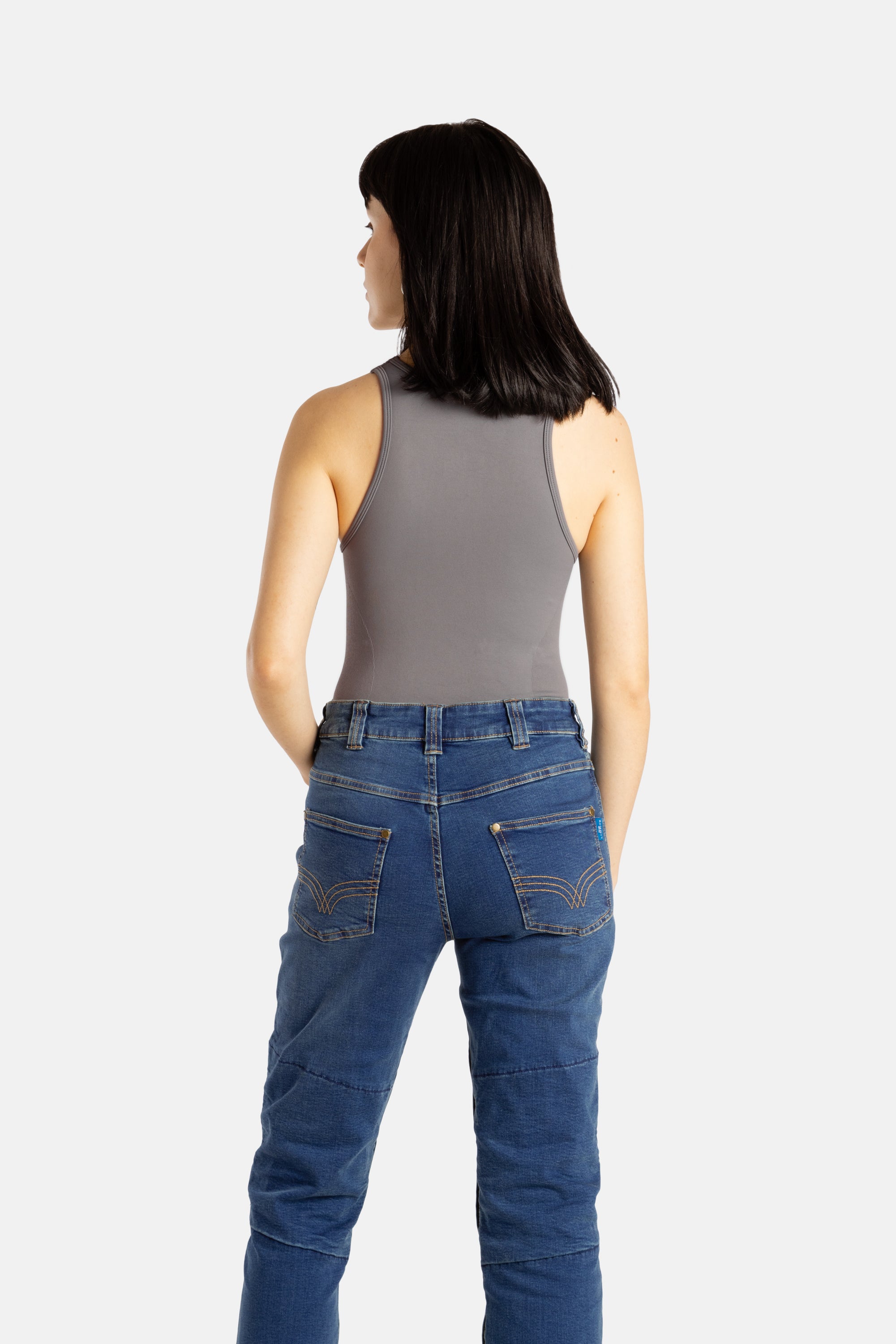 The back of a white woman with long black hair and hoop earrings wears a black tank top and denim jeans.