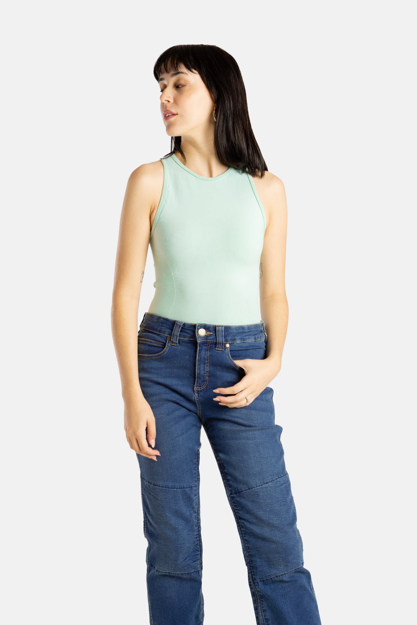 A white woman with long black hair and hoop earrings wears a sea form (Very light green) tank top and denim jeans.