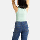 The back of a white woman with long black hair and hoop earrings wears a seaform (very light green) tank top and denim jeans.
