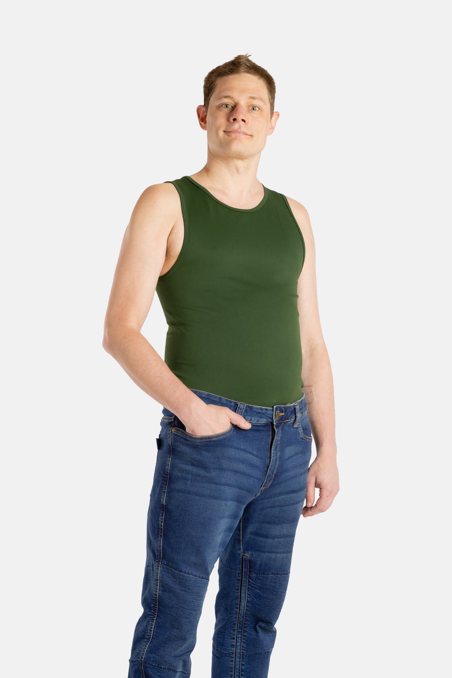 A white man with short brown hair wears an olive-green tank top and denim jeans.
