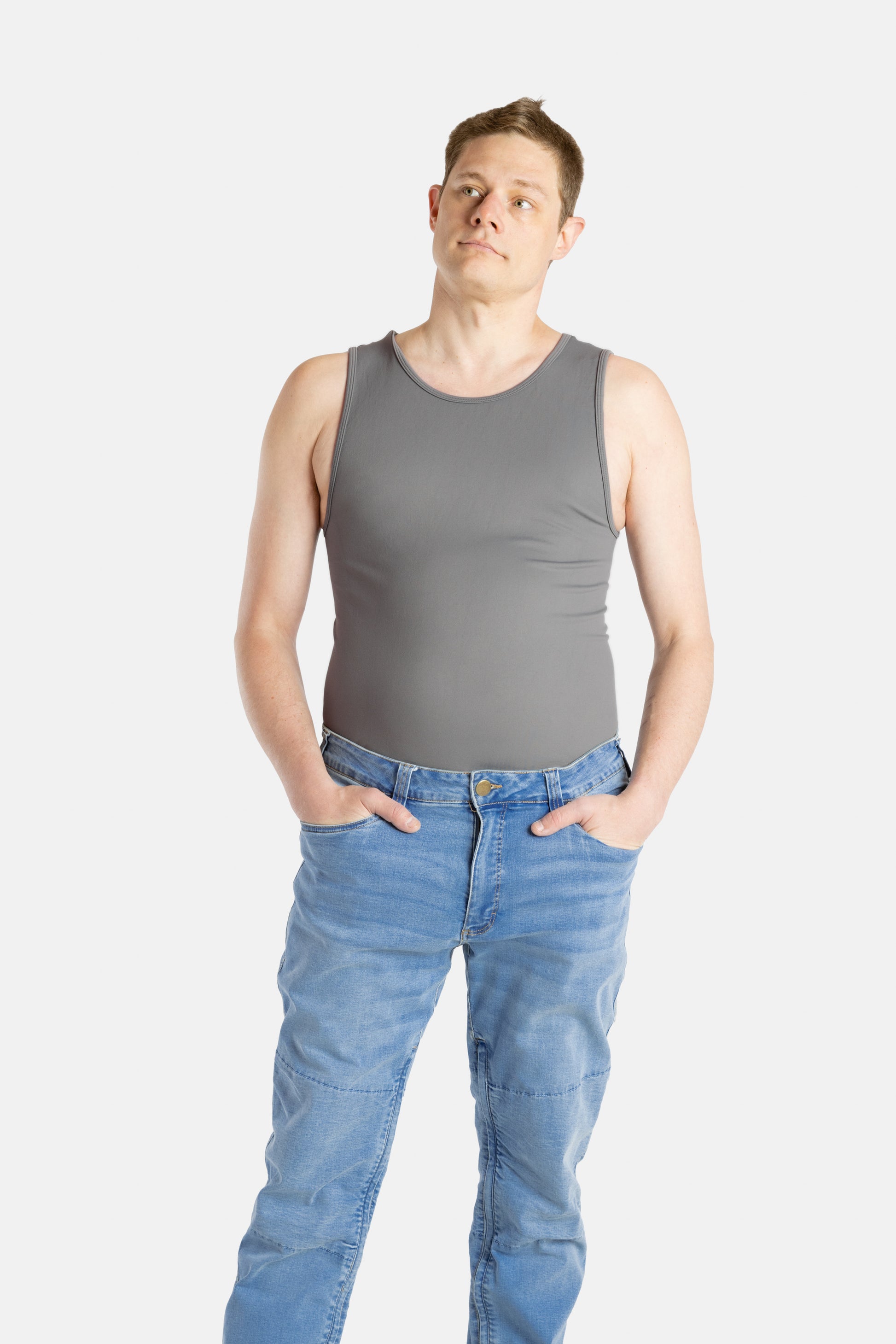 A white man with short brown hair wears a charcoal-gray tank top and denim jeans.