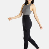 A white woman with long black hair and hoop earrings wears a charcoal tank top and black leggings.