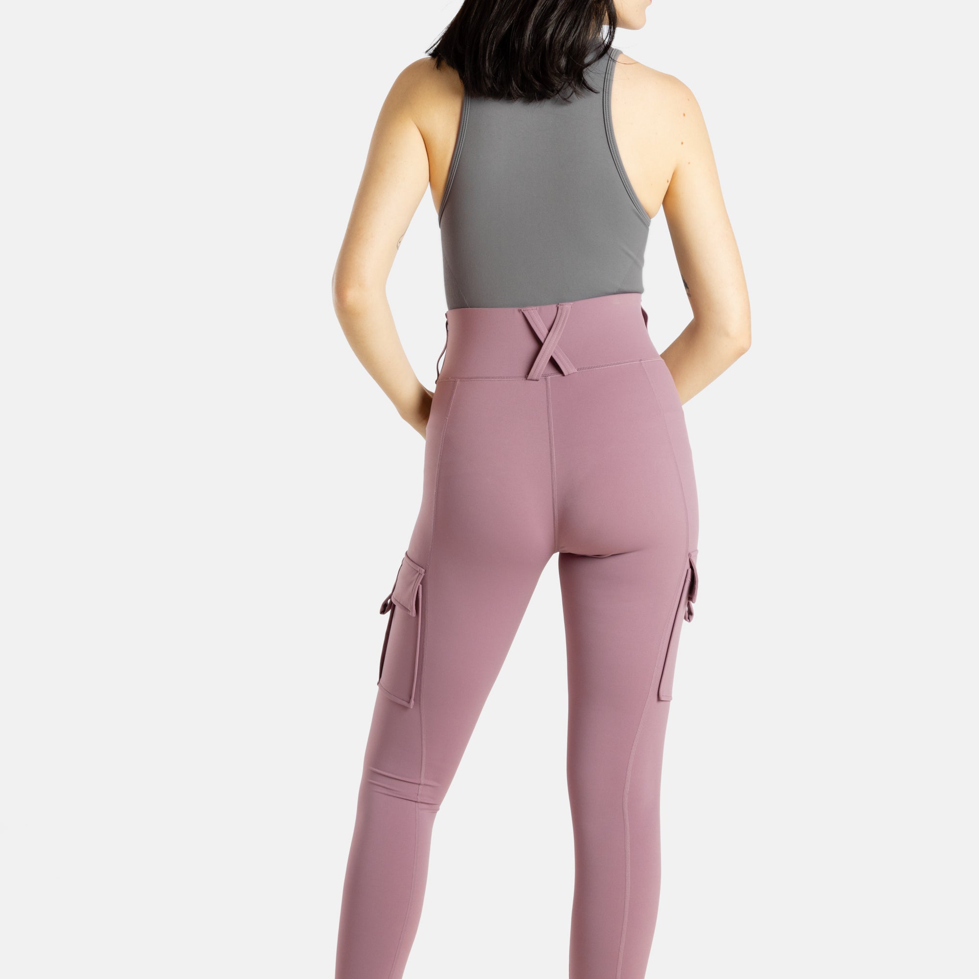 The back of a white woman (with long black hair and hoop earrings) wearing a charcoal tank top and mauve (Pinkish lavender) leggings.