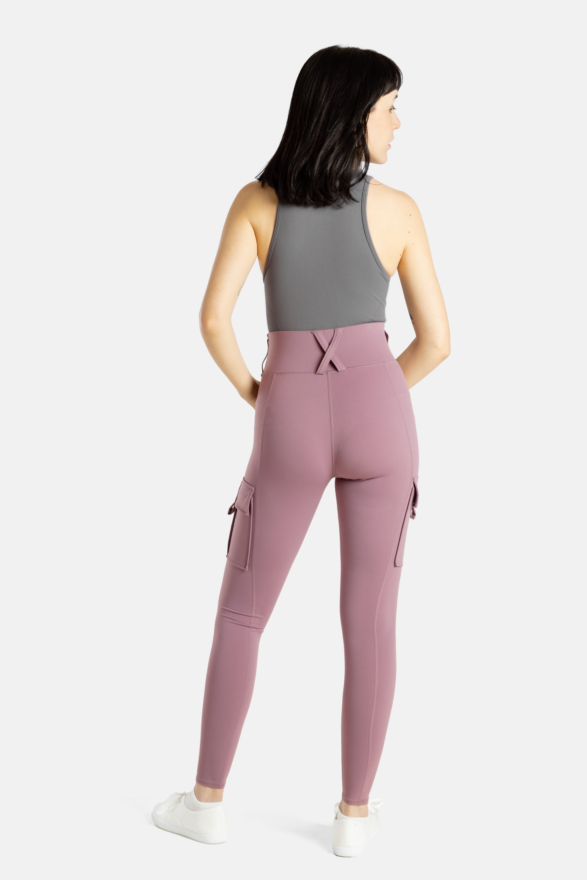 The back of a white woman (with long black hair and hoop earrings) wearing a charcoal tank top and mauve (Pinkish lavender) leggings.