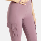 The close up of the mauve (Pinkish lavender) leggings. A hand is in the loop on the top of the pants. There are pockets on the legs.
