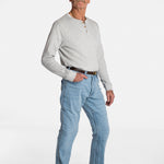 A white, elderly man with a mustache wears the Men’s Light Wash Unlimbited Pants, with a long-sleeved gray shirt, a brown belt, and brown shoes.