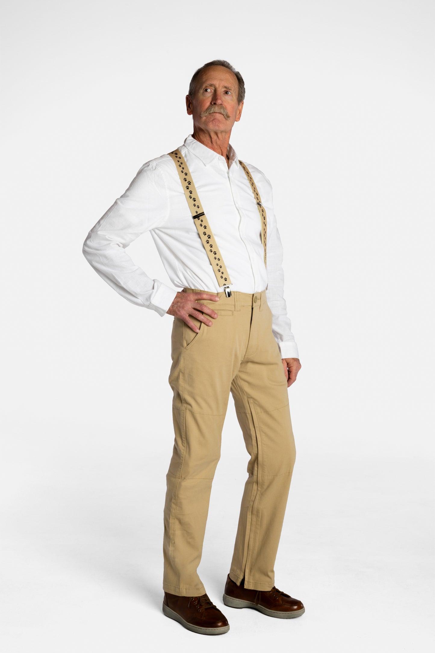 A white, elderly man with a mustache wears the No Limbits Adaptive Men's Khaki Unlimbited Pants, with a white shirt, tan suspenders, and brown shoes.