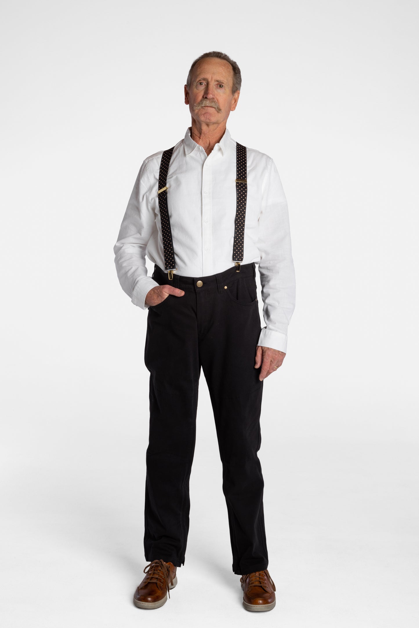 A white, elderly man with a mustache wears the No Limbits Adaptive Men's Black Unlimbited Pants, with a white shirt, brown suspenders, and brown shoes.