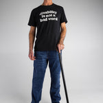 A old white man with a black cane wears navy t-shirt with cream text that says "disability is not a bad word."
