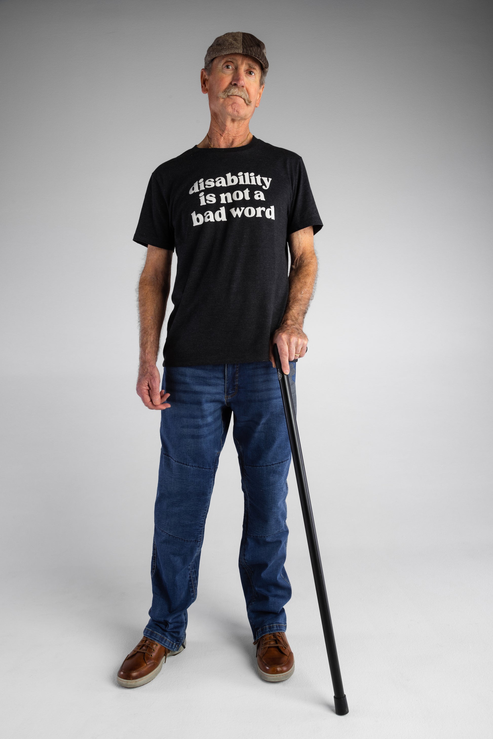 A old white man with a black cane wears navy t-shirt with cream text that says "disability is not a bad word."
