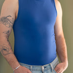 Close of a white man with a red beard and arm tattoos wearing a navy tank top and denim jeans.