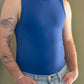 Close of a white man with a red beard and arm tattoos wearing a navy tank top and denim jeans.