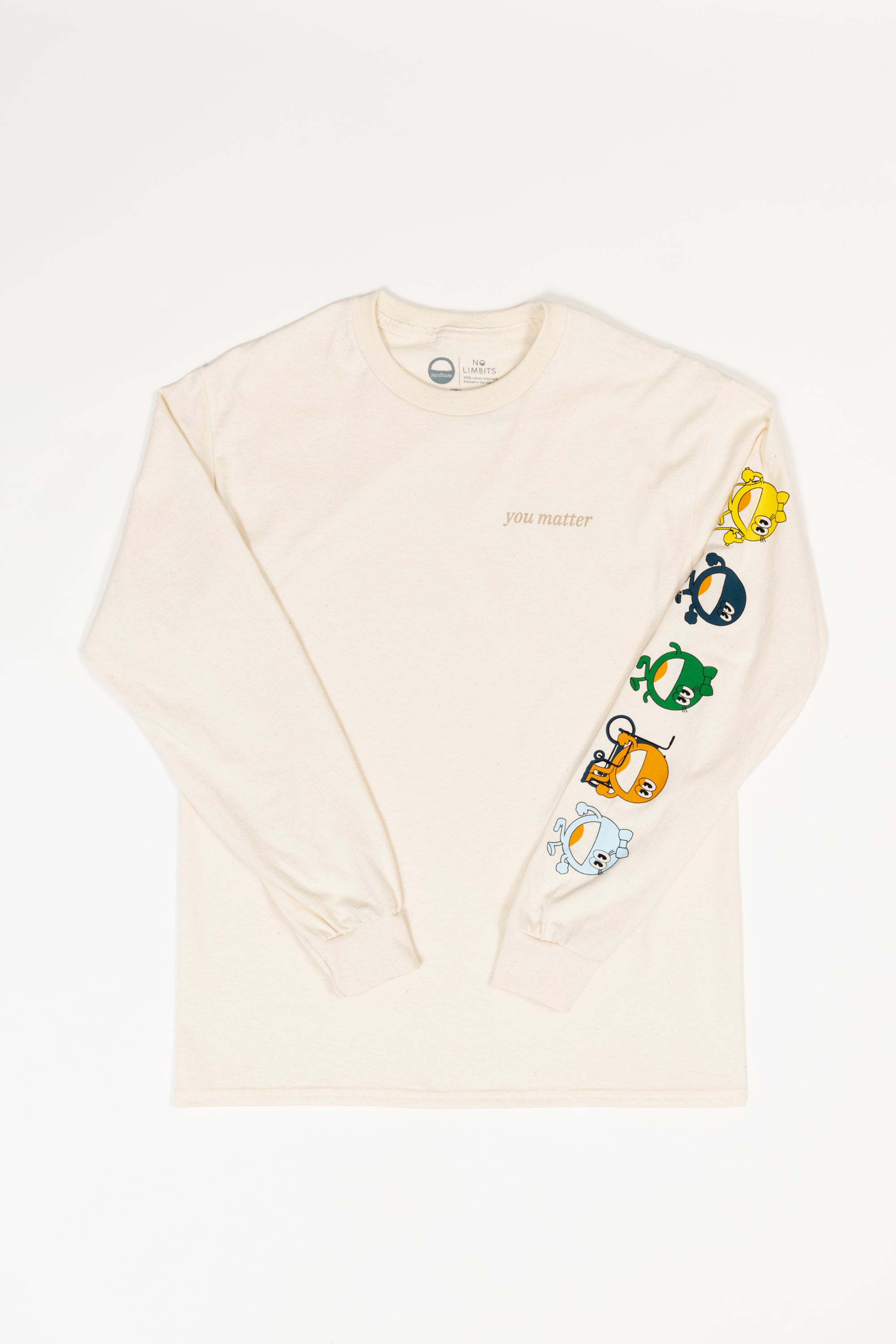 A flat lay of a long sleeve cream t-shirt. On the t-shirt it reads 'you matter' on a t-shirt standard pocket area. Running down the sleeve are characters walking down, they are a circle shape. The colors of the characters are yellow, navy, green, orange, and light blue.