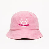 A light pink bucket hat with a white illustration of the sun and pink text that says "Unlimbited"